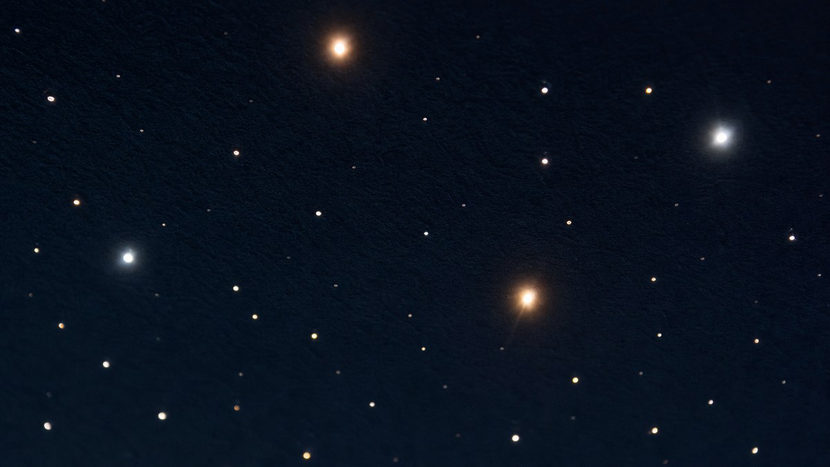 Close-up of fiber optic star tips of different diameters glowing as sharp pinpoint stars in a dark navy ceiling