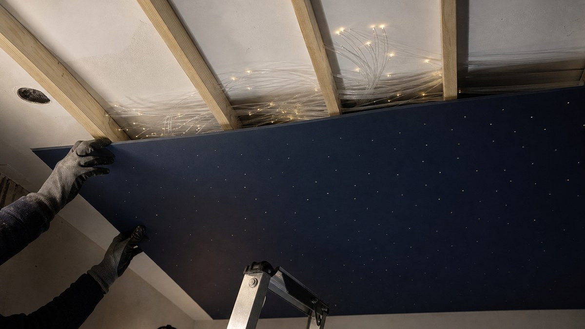 Installer attaching thin pre-drilled ceiling boards to furring strips with fiber optic strands routed in the shallow cavity, no attic above